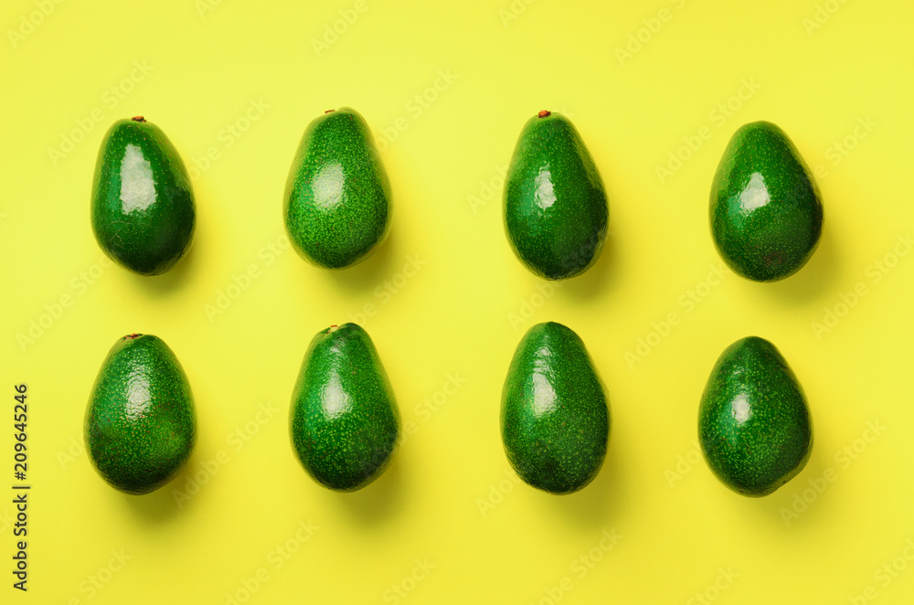 Green avocado pattern on yellow background. Top view. Pop art design, creative summer food concept. Organic avocadoes in minimal flat lay style. Green avocado pattern on yellow background. Top view. Pop art design, creative summer food concept. Organic avocadoes in minimal flat lay style.