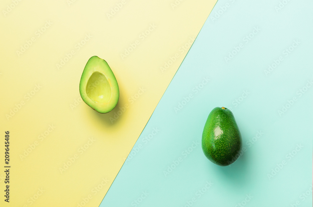 Avocado sliced with seed, whole fruit on blue and yellow background. Top view. Pop art design, creative summer food concept. Minimal flat lay style. Avocado sliced with seed, whole fruit on blue and yellow background. Top view. Pop art design, creative summer food concept. Minimal flat lay style.