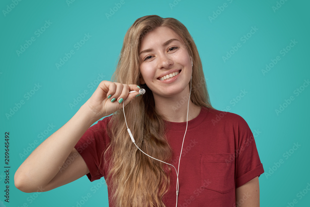 Image of blond cheerful woman wearing casual clothing singing while listening to music on smartphone via earphones isolated over blue background in studio Image of blond cheerful woman wearing casual clothing singing while listening to music on smartphone via earphones isolated over blue background in studio