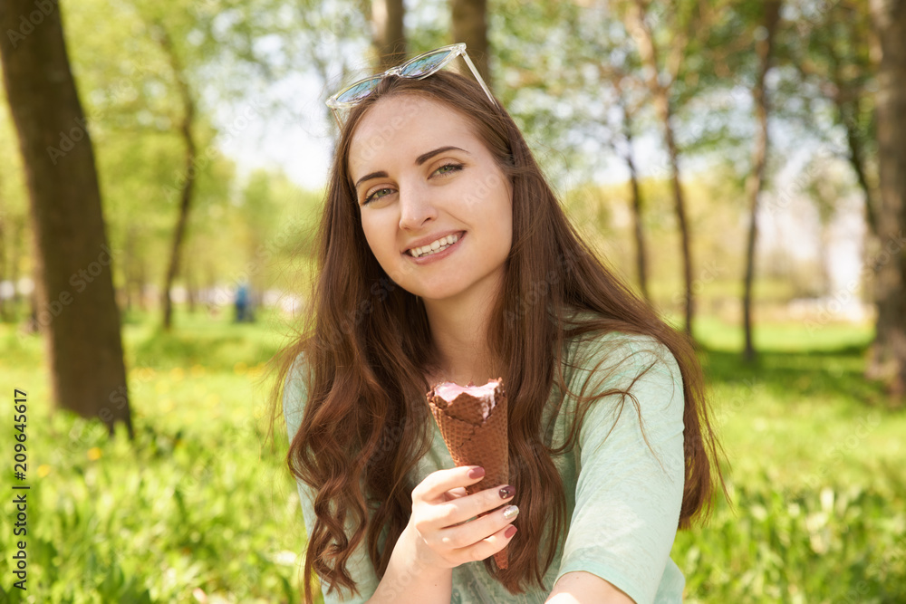 Portrait of beautiful young woman with light hair holding tasty ice-cream looking at it with great appetite wanting to eat it. People, summertime, relaxation and youth concept Portrait of beautiful young woman with light hair holding tasty ice-cream looking at it with great appetite wanting to eat it. People, summertime, relaxation and youth concept