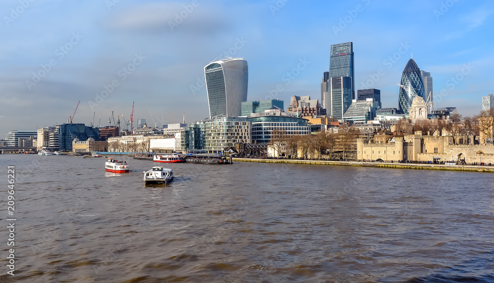 The City of London skyline, including boats in the Thames waters and famous London skyscrapers against blue winter sky.