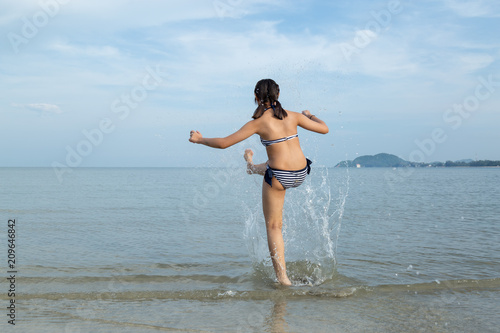Teenage wearing bikini kicks the sea water at the beach.