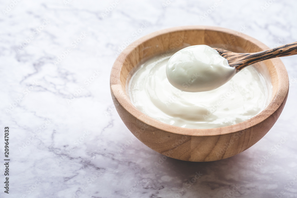 Yogurt in wooden bowl on marble table Yogurt in wooden bowl on marble table