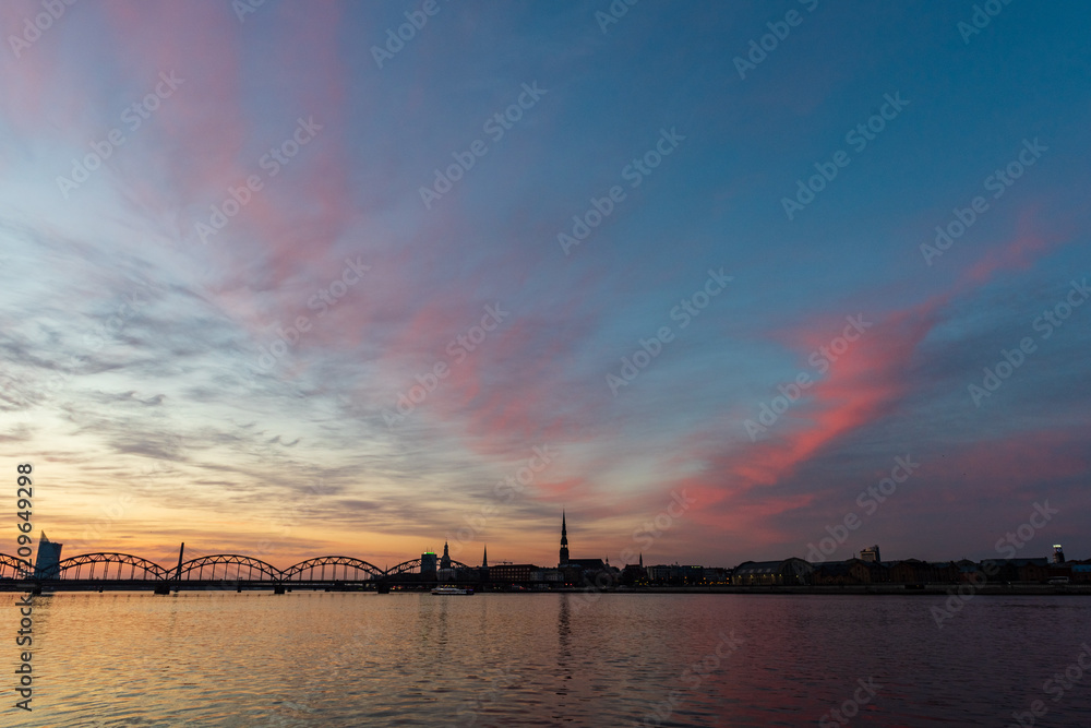 railroad metal bridge silhouette over river of Daugava in Riga, Latvia in dark red sunet