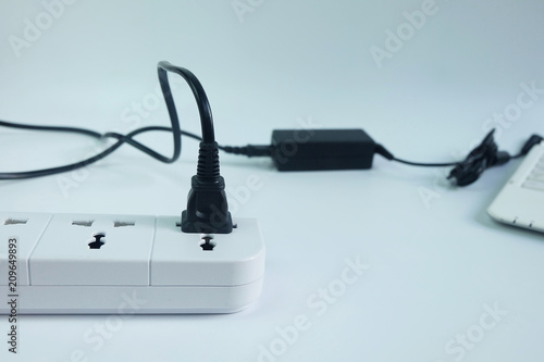 Close up plug in Adapter power cord charger with blurred laptop computer on white background