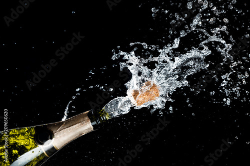 Celebration of birthday, anniversary or Christmas theme. Explosion of splashing champagne sparkling wine with flying cork out of the bottle on black background. photo
