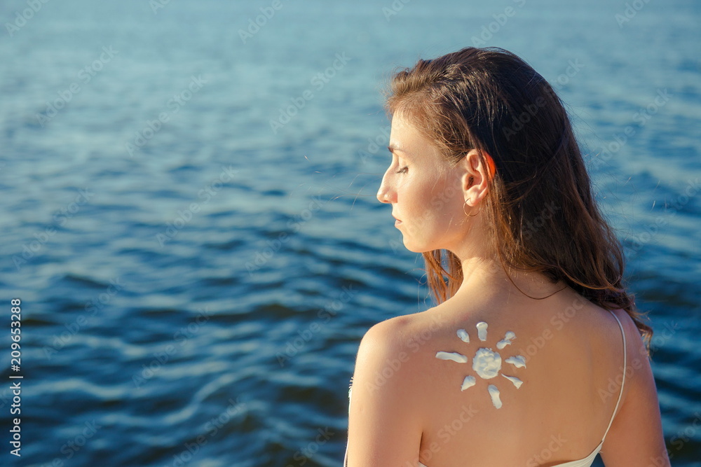 Sunbath protection. Woman using sun cream on the beach. Sun on a girl's shoulder, Sun-shaped cream on a young woman's skin. Portrait woman on  sea background

