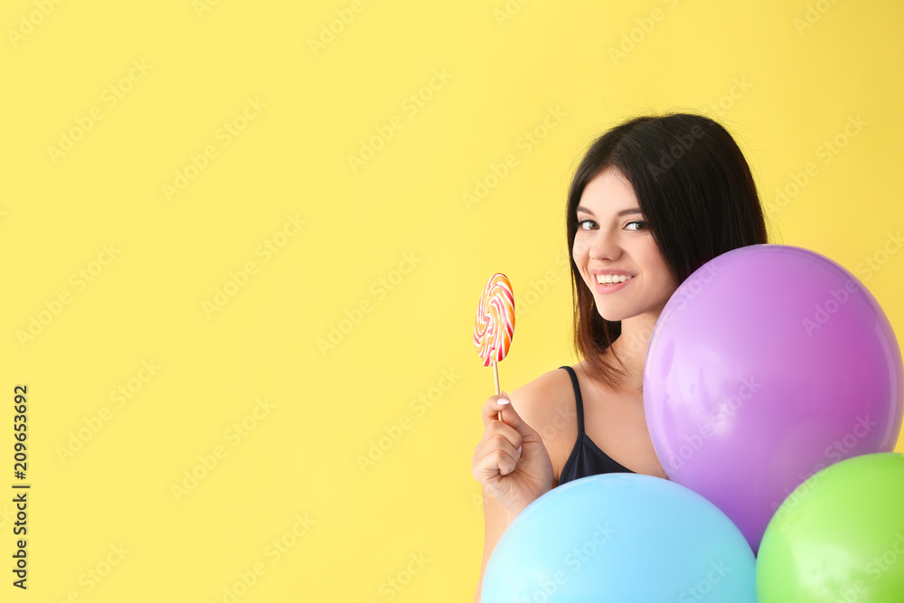 Beautiful young woman with lollipop and balloons on color background