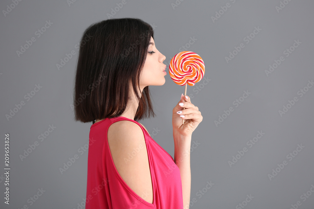 Beautiful young woman with lollipop on grey background
