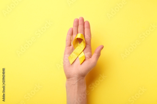 Female hand holding yellow ribbon on color background. Cancer concept