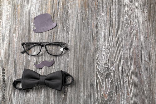 Festive composition with eyeglasses, paper hat, moustache and bow tie on wooden background. Happy Father's Day