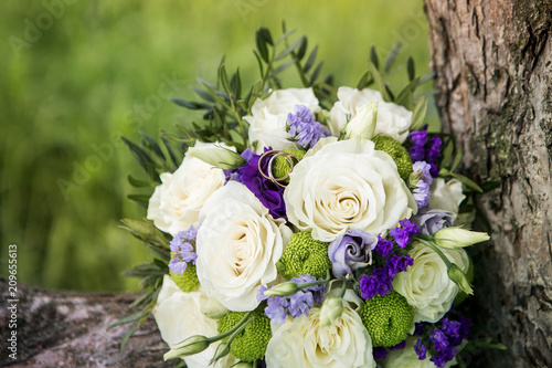 White roses with blue and lavender flowers bouquet. Wedding ring macro photography. Beautiful bridal bouquet with white roses and golden rings
