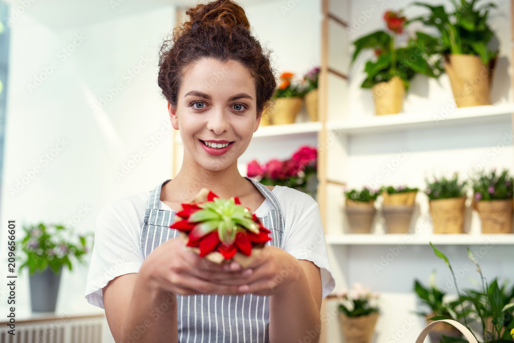 Shop assistant. Cheerful young woman selling a plant while working as a shop assistant