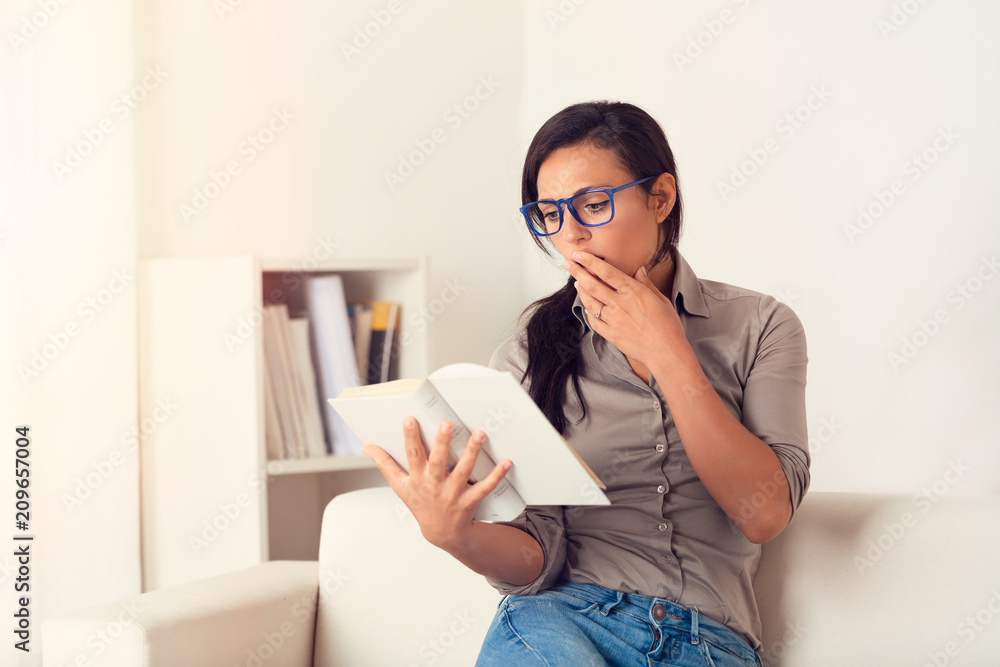 Astonished Woman reading a book on couch at home Astonished Woman reading a book on couch at home