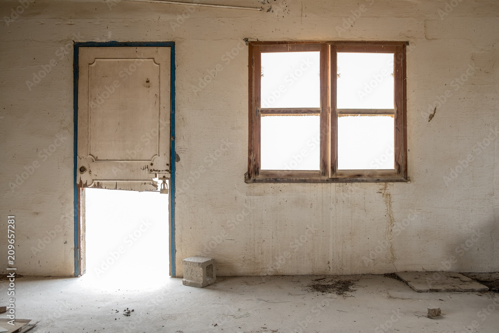 A window and broken door in the wall of a room in an abandoned, derelict building with stained walls. A window and broken door in the wall of a room in an abandoned, derelict building with stained walls.