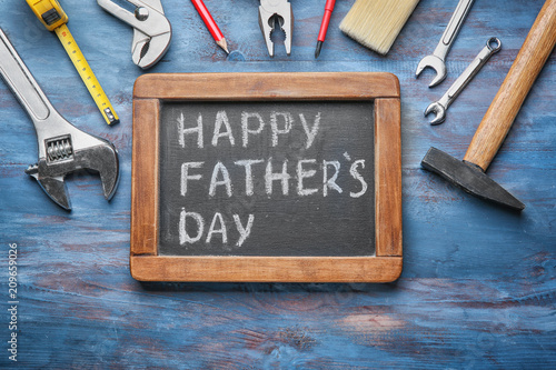 Chalkboard with text "Happy Father's Day" and set of tools on wooden background