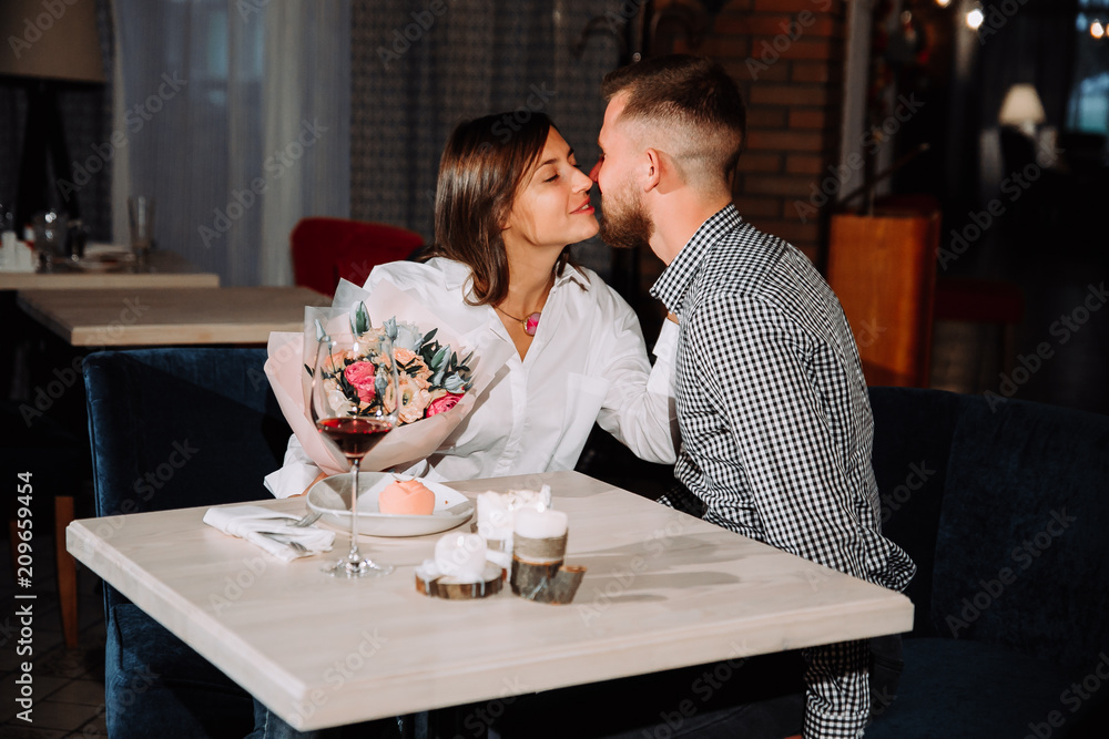 Happy romantic couple in cafe. Young man is presenting flowers to his beloved. Happy romantic couple in cafe. Young man is presenting flowers to his beloved.