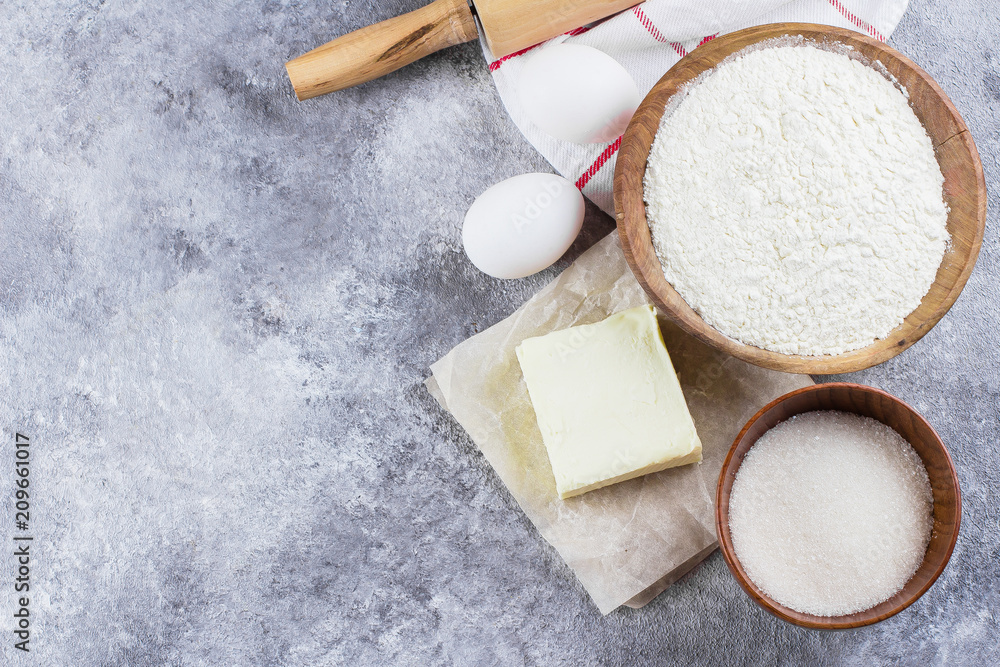 Baking ingredients for cake, pie, shortbread pastry: flour, eggs, sugar, butter, rolling pin and on gray concrete table background. Top view, copy space Baking ingredients for cake, pie, shortbread pastry: flour, eggs, sugar, butter, rolling pin and on gray concrete table background. Top view, copy space