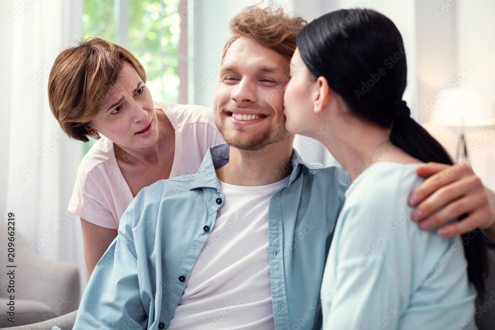 Family member. Unhappy aged woman looking at the couple while not approving their relationships Family member. Unhappy aged woman looking at the couple while not approving their relationships