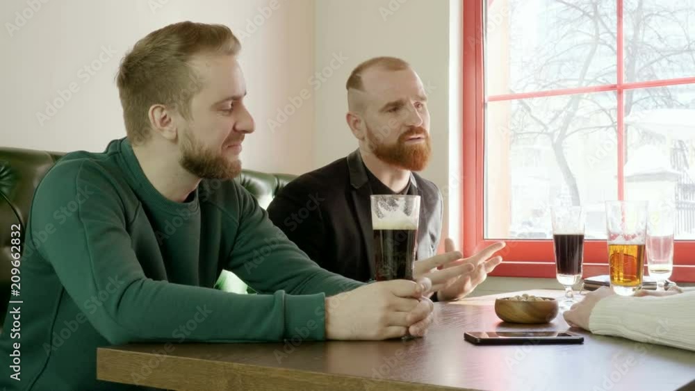 Weekend activities. Three friends drinking draft beer and talking in a pub. 4K Weekend activities. Three friends drinking draft beer and talking in a pub. 4K