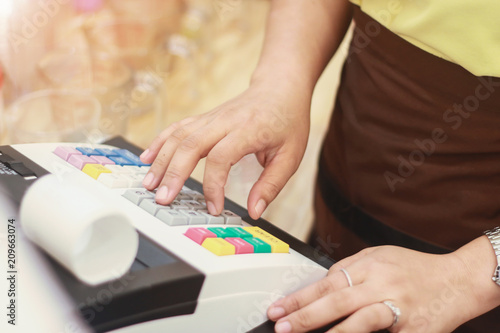 Sales women entering amount on cash register in offee shop