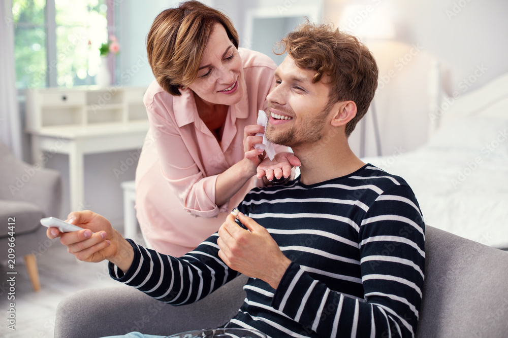 Pleasurable relaxation. Joyful pleasant man resting at home while enjoying attention of his mother Pleasurable relaxation. Joyful pleasant man resting at home while enjoying attention of his mother