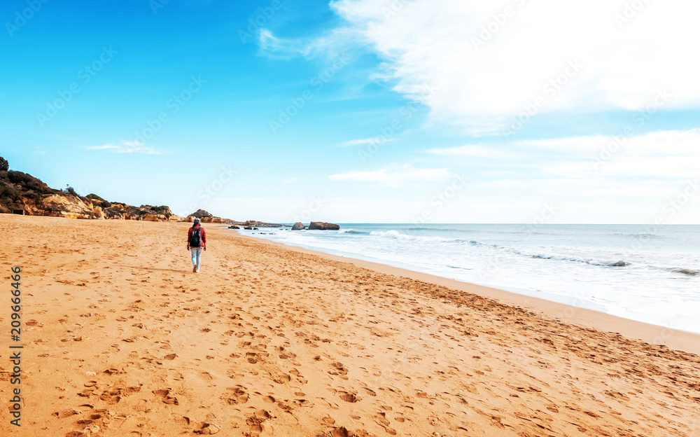 Girl traveler with a backpack walking along a sandy beach along the ocean coast