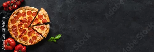 Obraz  z motywem Tasty pepperoni pizza and cooking ingredients tomatoes basil on black concrete background. Top view of hot pepperoni pizza. Banner
