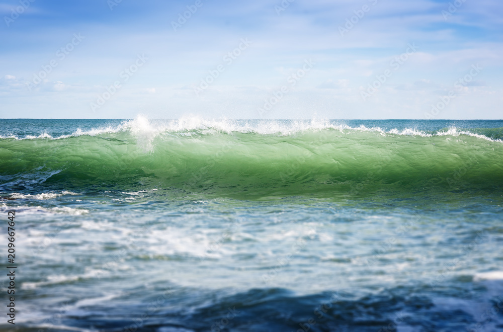 Fototapeta premium A beautiful seascape, a turquoise wave with splashes rolls to the shore, a natural background and a texture