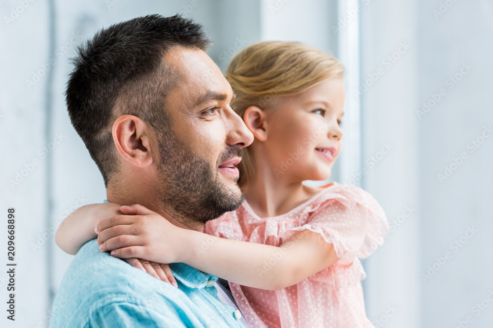 happy father carrying adorable little daughter and looking away at home happy father carrying adorable little daughter and looking away at home