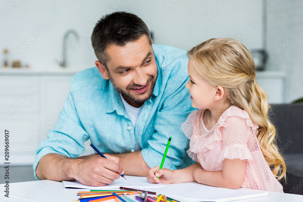 happy father and daughter smiling each other while drawing together at home happy father and daughter smiling each other while drawing together at home