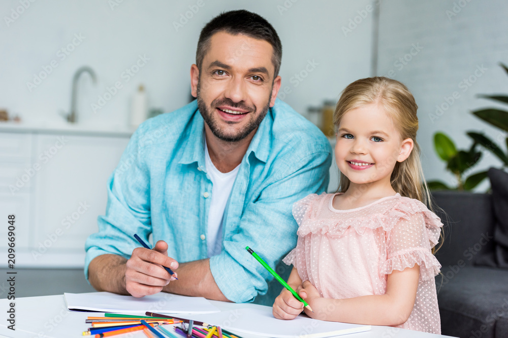 happy father and daughter drawing with colored pencils and smiling at camera