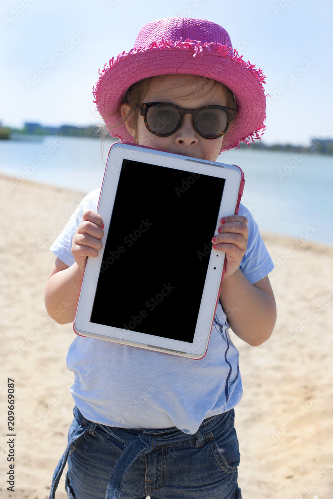 Little girl with a tablet computer in hands. Good summer weekend on the beach. Copy spce.