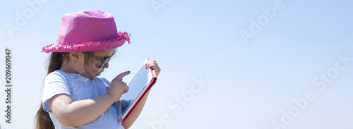 Little girl with a tablet computer in hands. Good summer weekend on the beach. Copy spce