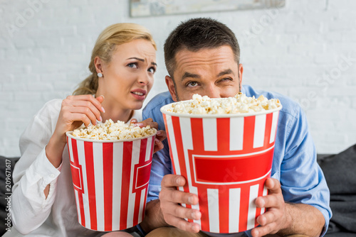 emotional couple holding popcorn boxes while watching tv at home