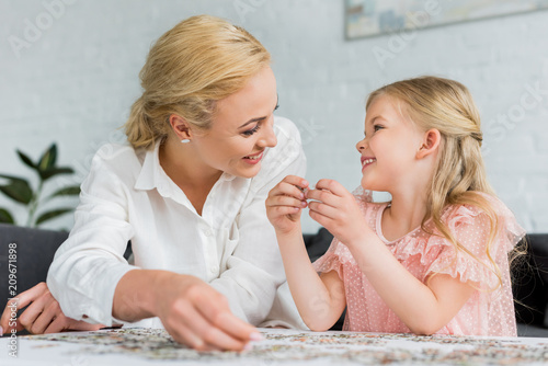 happy mother and daughter smiling each other while playing with puzzle pieces at home
