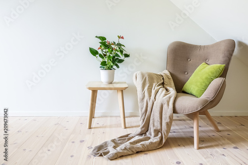 Obraz na plátně Beige armchair with a green pillow, blanket and a wooden table with a potted plant (Anthurium)