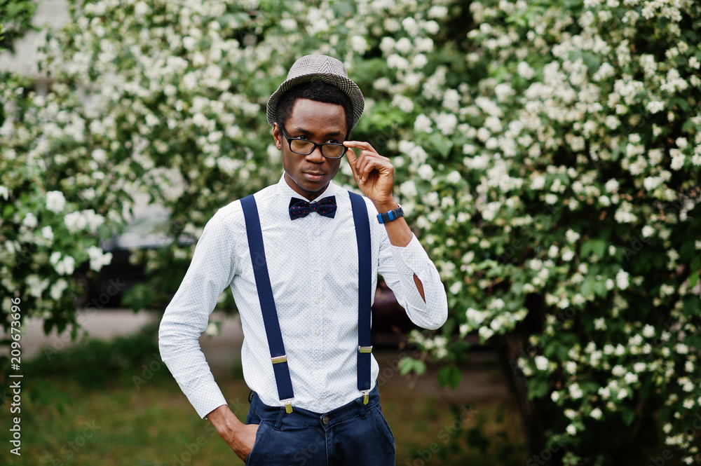 Stylish african american business man at pants with suspender and shirt with bow tie, hat and glasses posed outdoor. Stylish african american business man at pants with suspender and shirt with bow tie, hat and glasses posed outdoor.