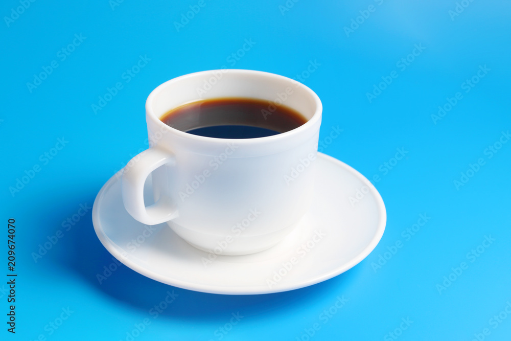 White cup with black coffee on a saucer on a blue background White cup with black coffee on a saucer on a blue background