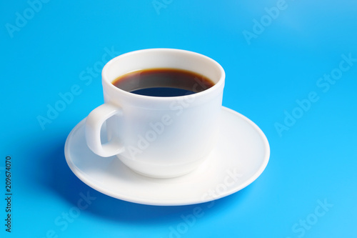 White cup with black coffee on a saucer on a blue background