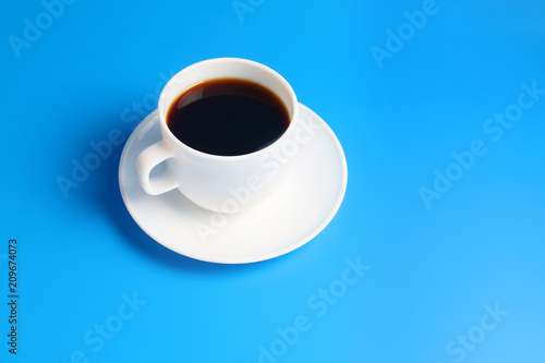 Simple white cup with black coffee on a saucer on a blue background