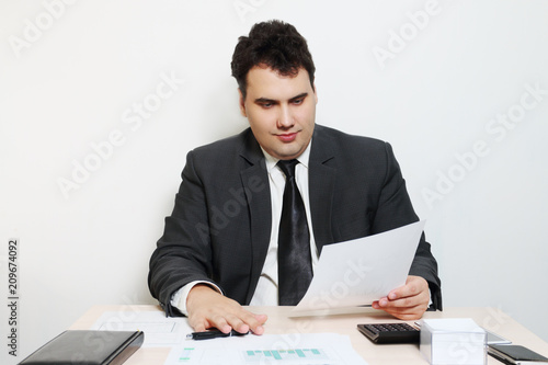 Smiling businessman in suit looks at document at table with notebook, paper, pen