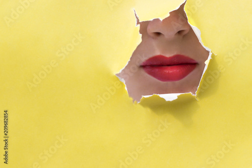 Red lips through look in the torn slot of yellow paper, copy space photo