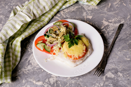 Fish baked with cheese and tomatoes on a white plate
