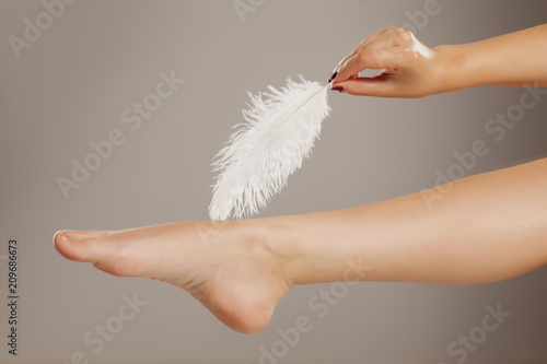 well-nourished woman leg and a white feather on a gray background photo