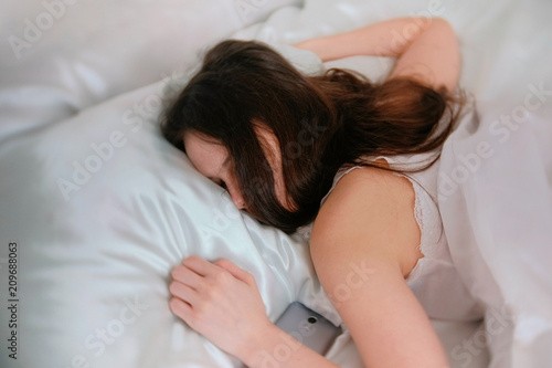 Young woman brunette sleeping in bed. Mobile phone near her.