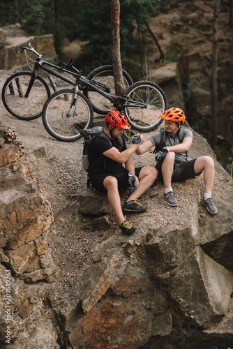 high angle view of young trial bikers relaxing on rocky cliff after ride and shaking hands