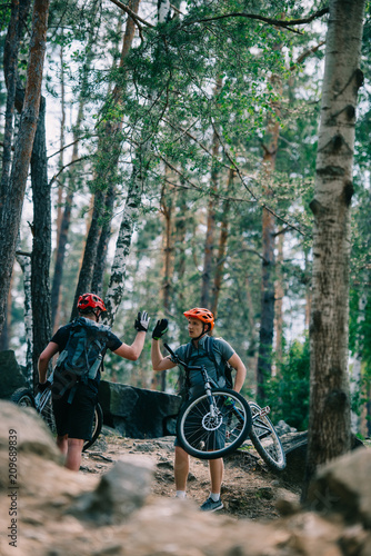 young trial bikers giving high five at beautiful forest