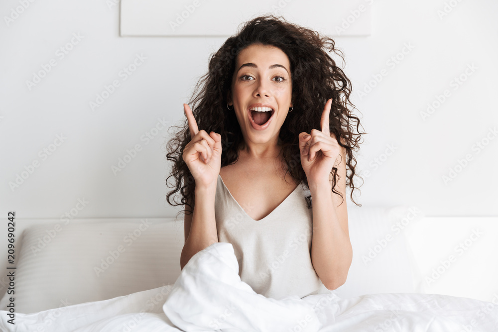 Happy young girl with dark curly hair sitting in bed Happy young girl with dark curly hair sitting in bed