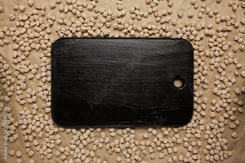 Black cutting board on crumpled brown paper with chickpea. Top view, space for text.